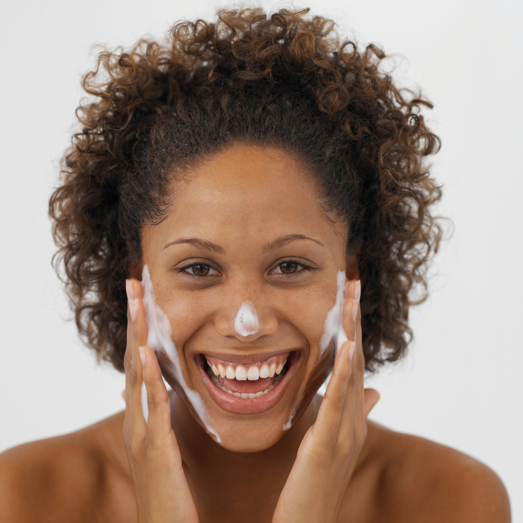 Close-up of a smiling woman washing her face with soap